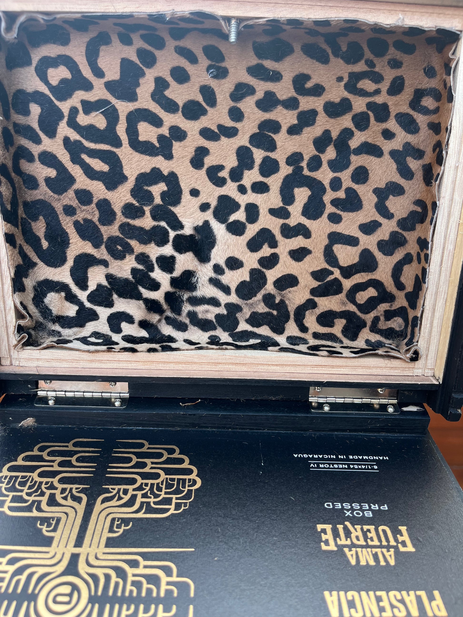 Leopard print fabric in a box with a black book featuring gold text on a wooden surface.